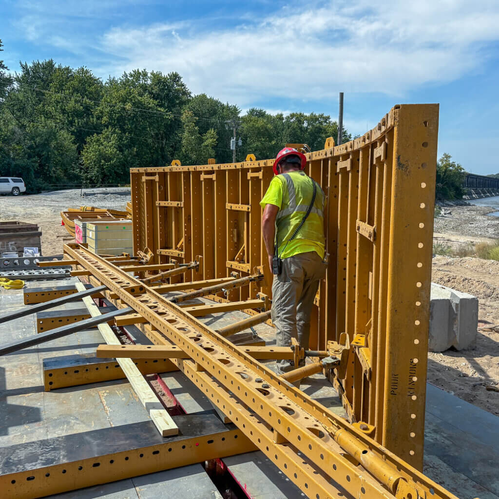 Crew member walking along the steel REDI-RADIUS® form set on its side. The same structural backbone that keeps the forms rigid during placement also serves as the picking frame for crane operations, simplifying the entire forming sequence.